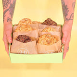 Hands holding a green box of 6 x New York Cookies, The Nutty Box by Crumbs & Doilies in paper sleeves.